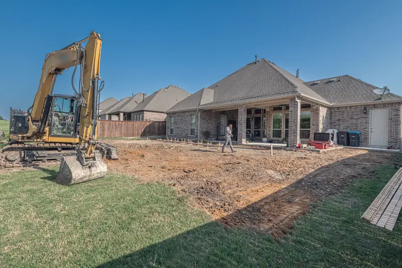Small excavator digging in the back yard of a brick house